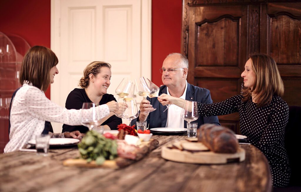 Die drei Bremer-Schwestern sitzen mit Herrn Acker am Tisch und stoßen mit Wein an
