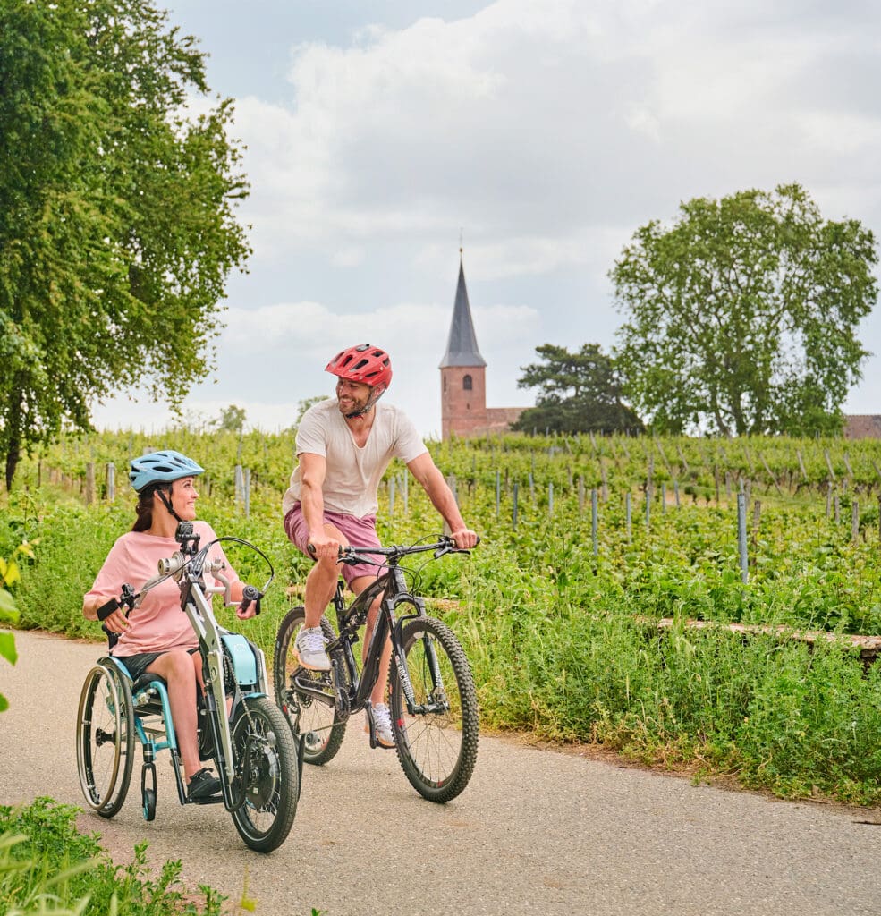 Eine Frau auf einem Rollstuhlfahrrad und ein Mann auf einem Mountainbike fahren durch die Weinberge