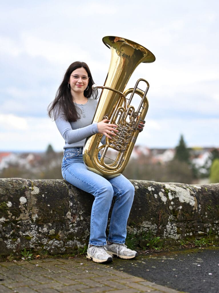 Mia Wradatsch sitzt mit ihrer Tuba auf einer Mauer.